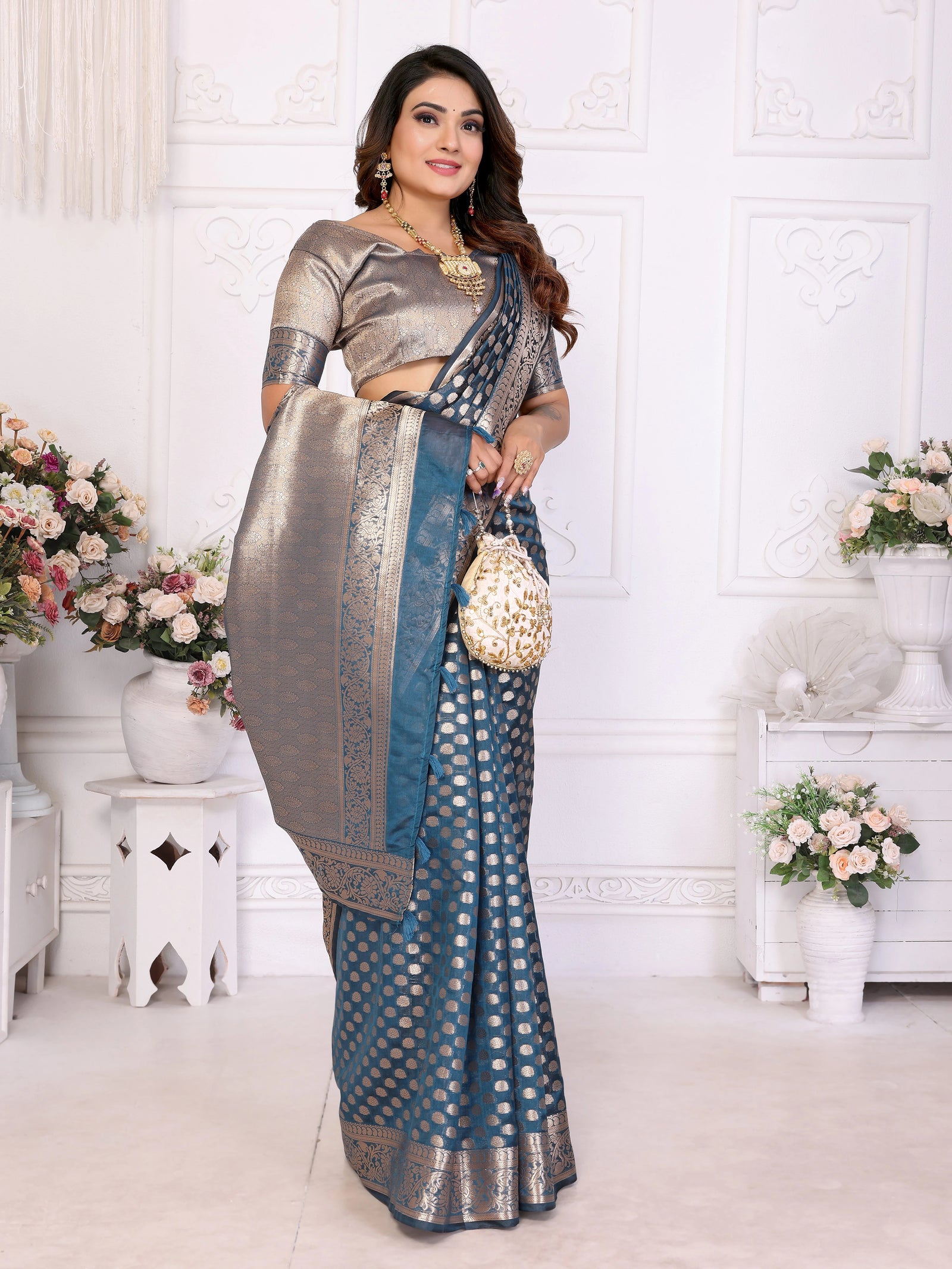 Woman wearing a traditional saree in a decorated room with flowers and white furniture.