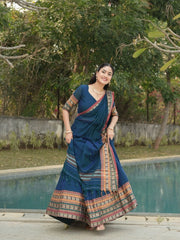 Woman in a blue saree with a colorful border standing by a pool with greenery in the background