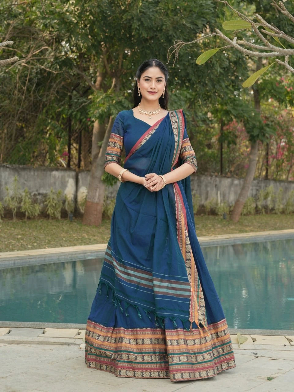 Woman in a blue saree with a pool and greenery in the background