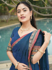 Woman in a blue saree with gold jewelry standing by a pool.