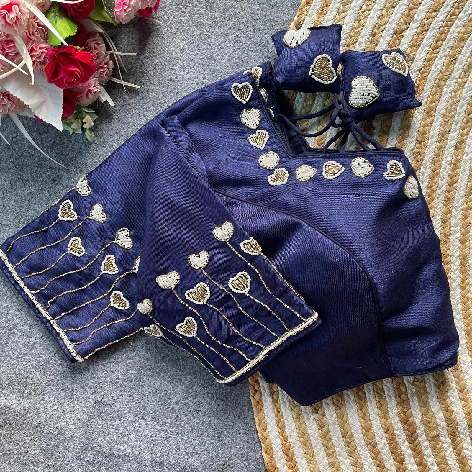 Navy blue blouse with gold heart embroidery on a textured surface with flowers.