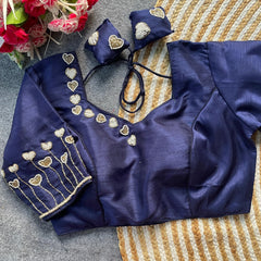 Navy blue blouse with gold embroidery on a textured surface with flowers in the background