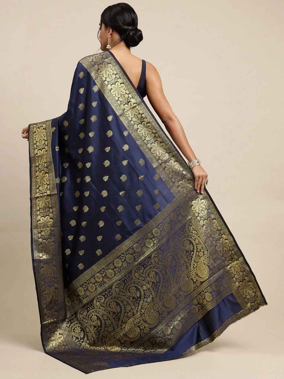 Woman wearing a navy blue saree with gold patterns on a beige background