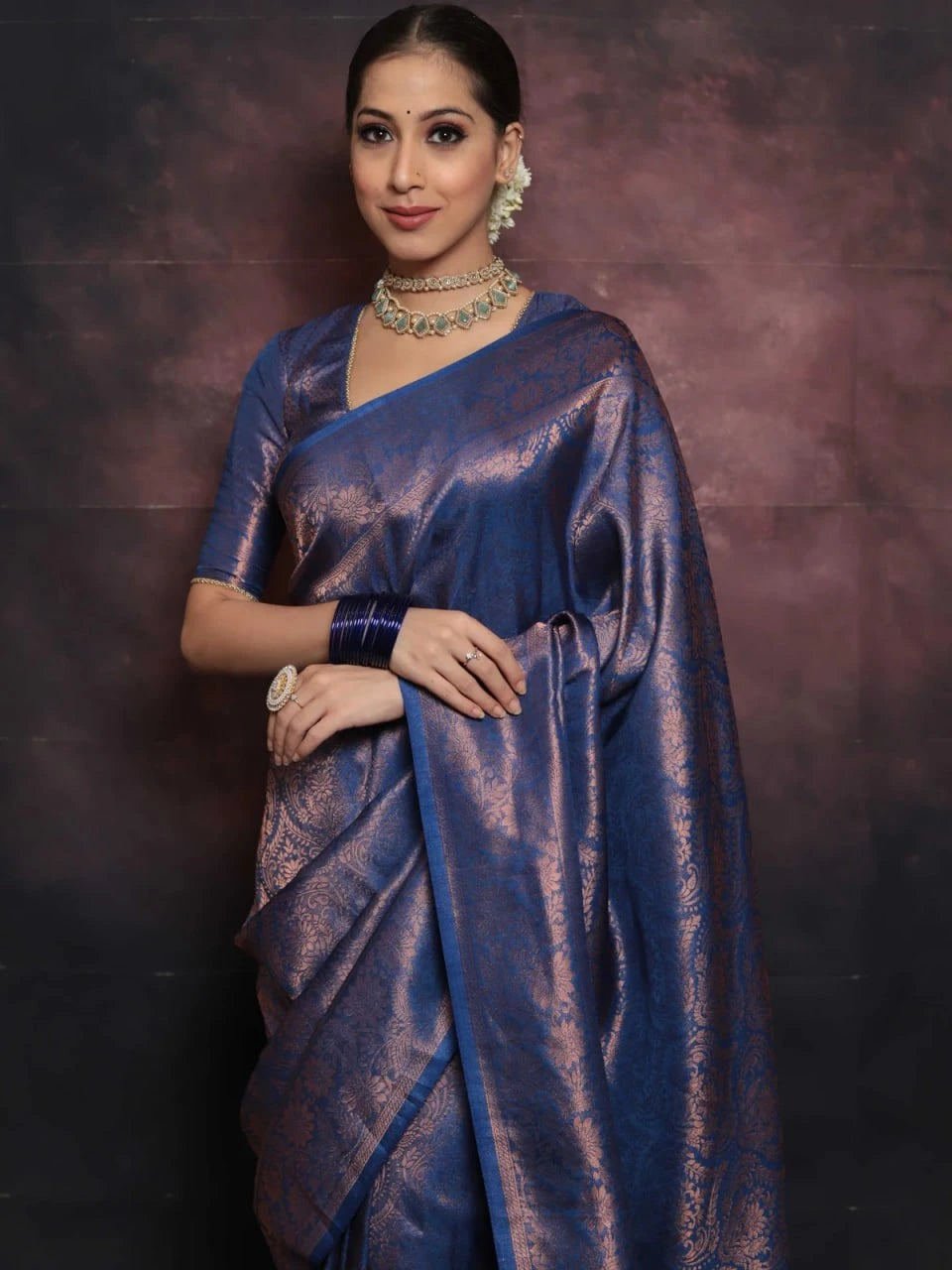 Woman wearing a blue saree with jewelry against a dark background
