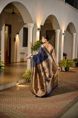 Woman in a traditional saree walking in an outdoor setting with arches and plants.
