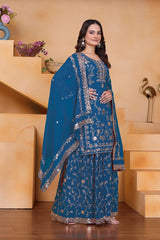 Woman wearing a blue embroidered traditional outfit in a decorated room.