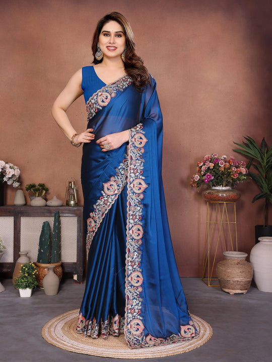 Woman wearing a blue saree with floral patterns in an indoor setting.