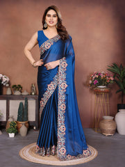 Woman wearing a blue saree with floral patterns in an indoor setting.