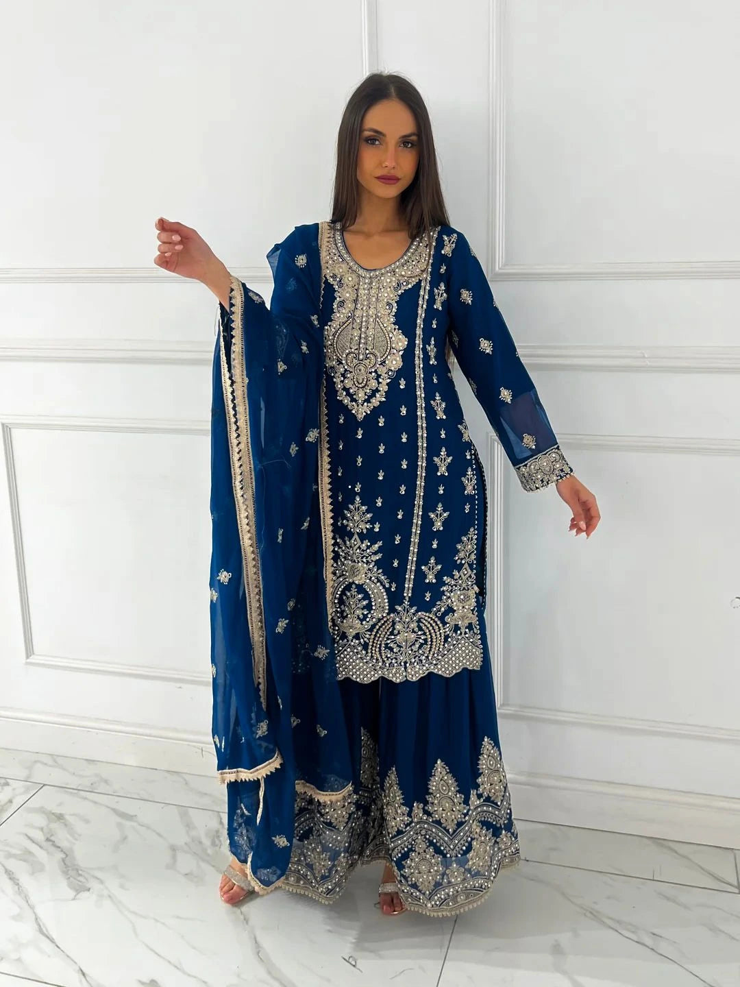 Woman wearing a blue embroidered traditional outfit with a white background