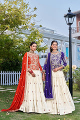 Two women in traditional outfits standing outdoors with a building and trees in the background.