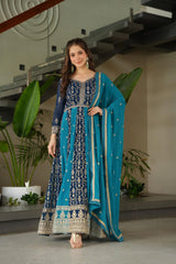 Woman in a blue and navy traditional outfit standing indoors with plants in the background