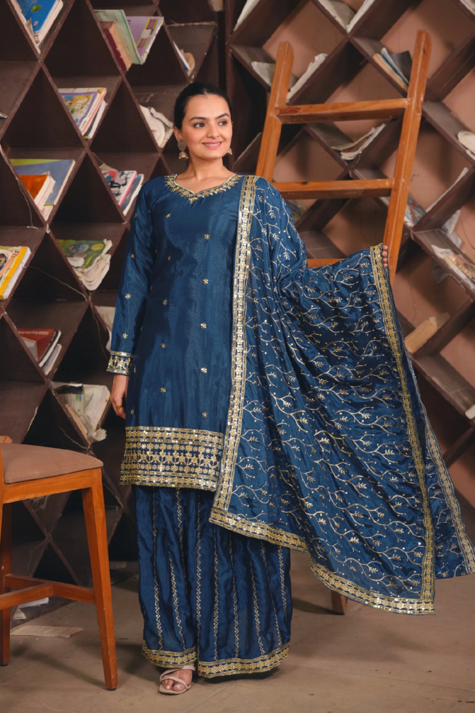 Woman in a blue traditional outfit standing in front of a bookshelf.
