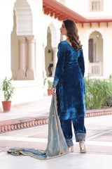 Woman in a blue traditional outfit standing in front of a building with architectural elements.