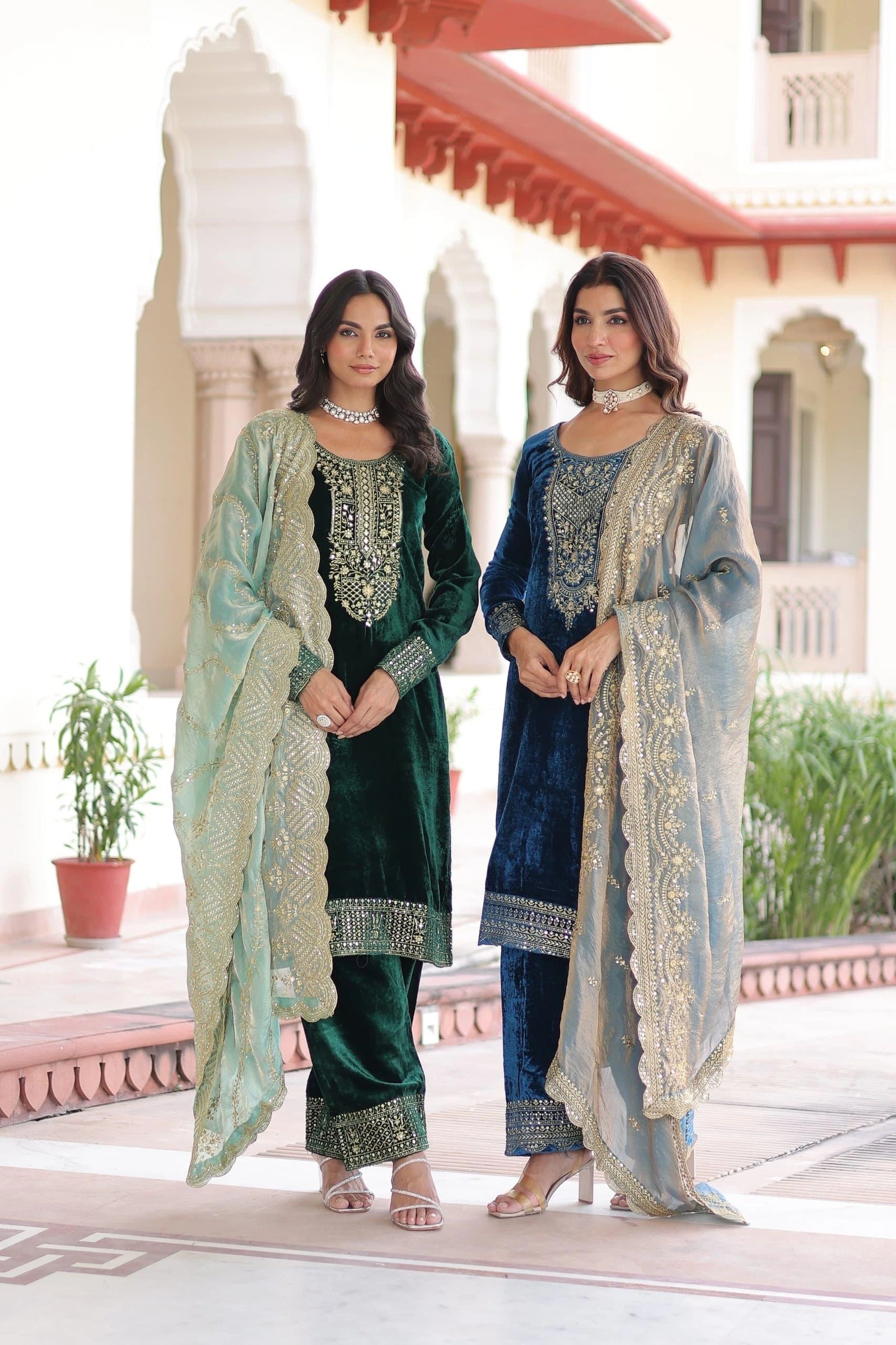 Two women in traditional outfits standing in front of a building with decorative elements.