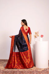 Woman wearing a traditional saree with a red and blue pattern, standing against a plain background.