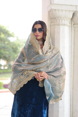 Woman wearing a large, ornate shawl with intricate patterns in an outdoor setting.