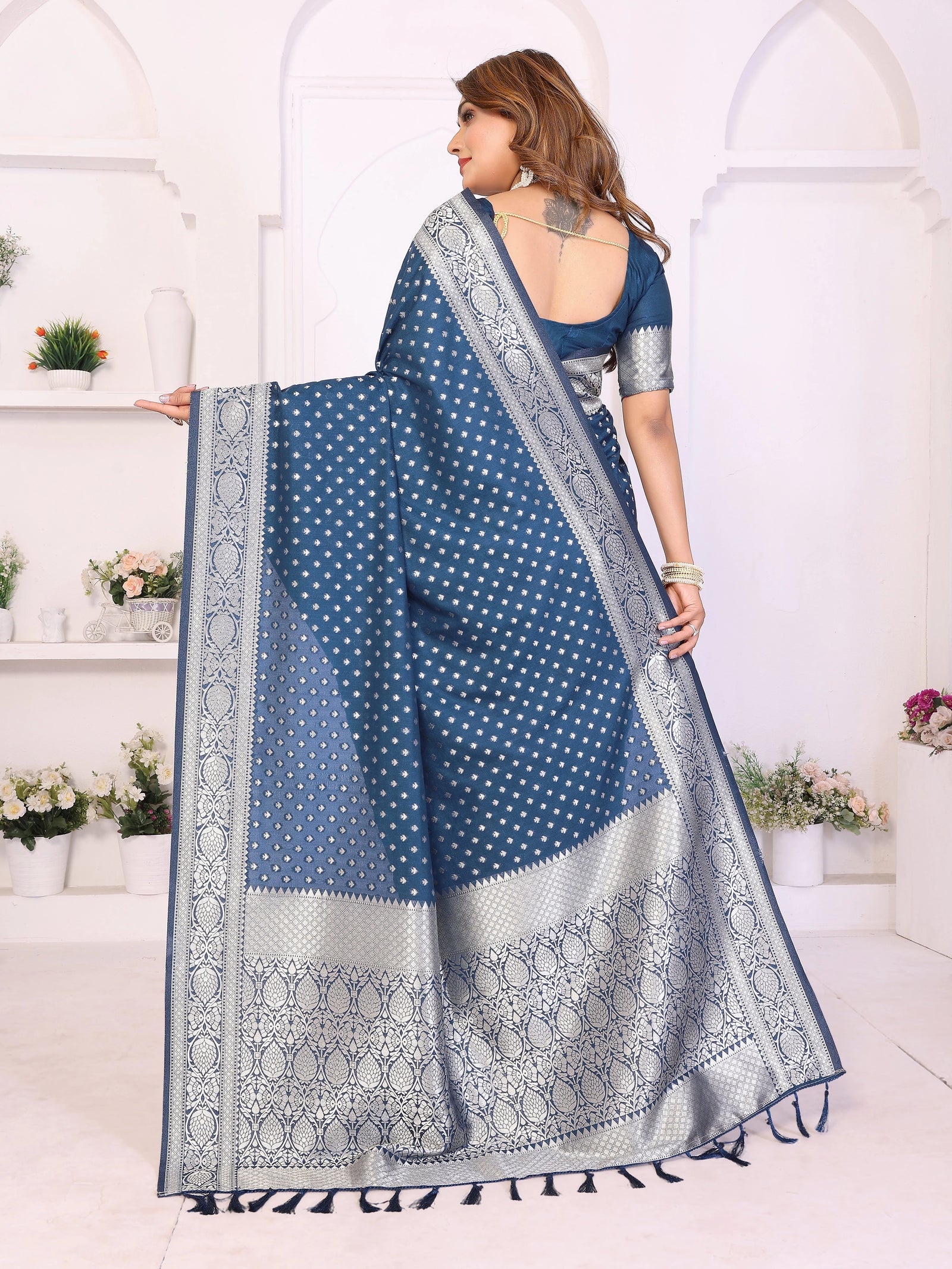 Woman wearing a blue saree with white patterns in a white room.