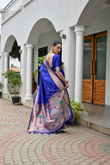 Woman in a blue and pink saree standing in front of a white building with columns.