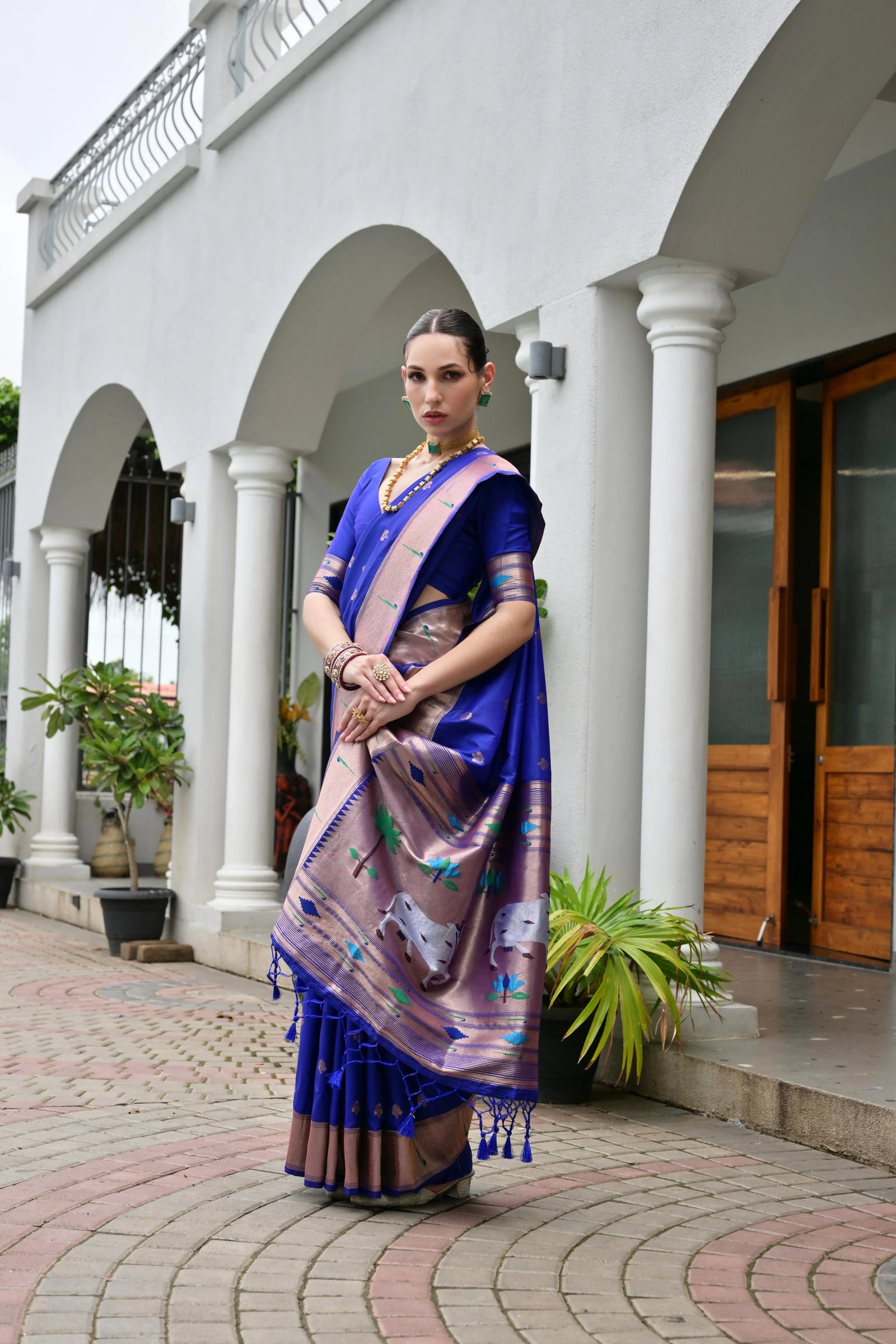 Woman in a blue saree with a patterned border standing in front of a white building.