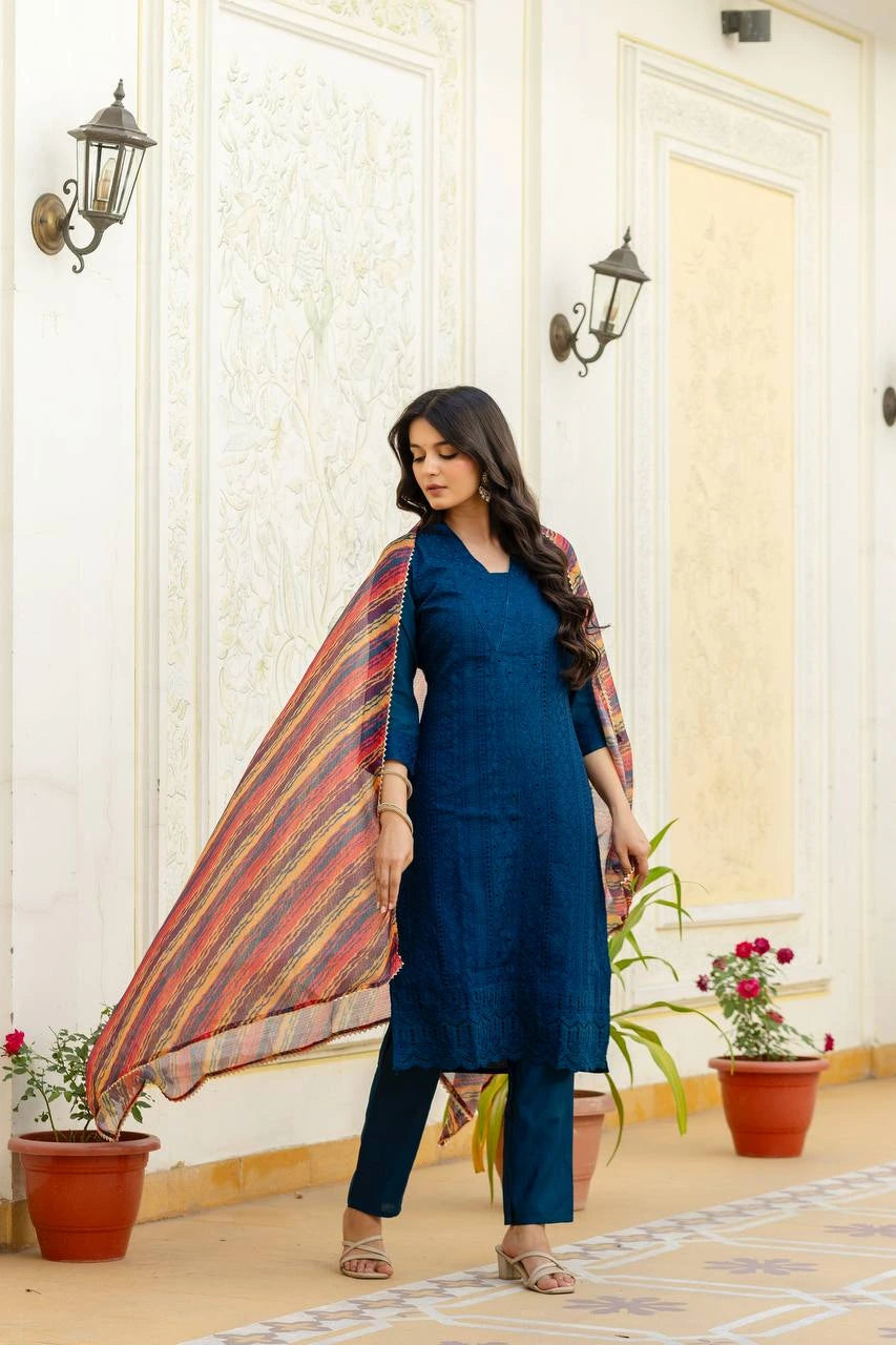 Woman in a blue outfit with a colorful scarf standing in a decorated room.