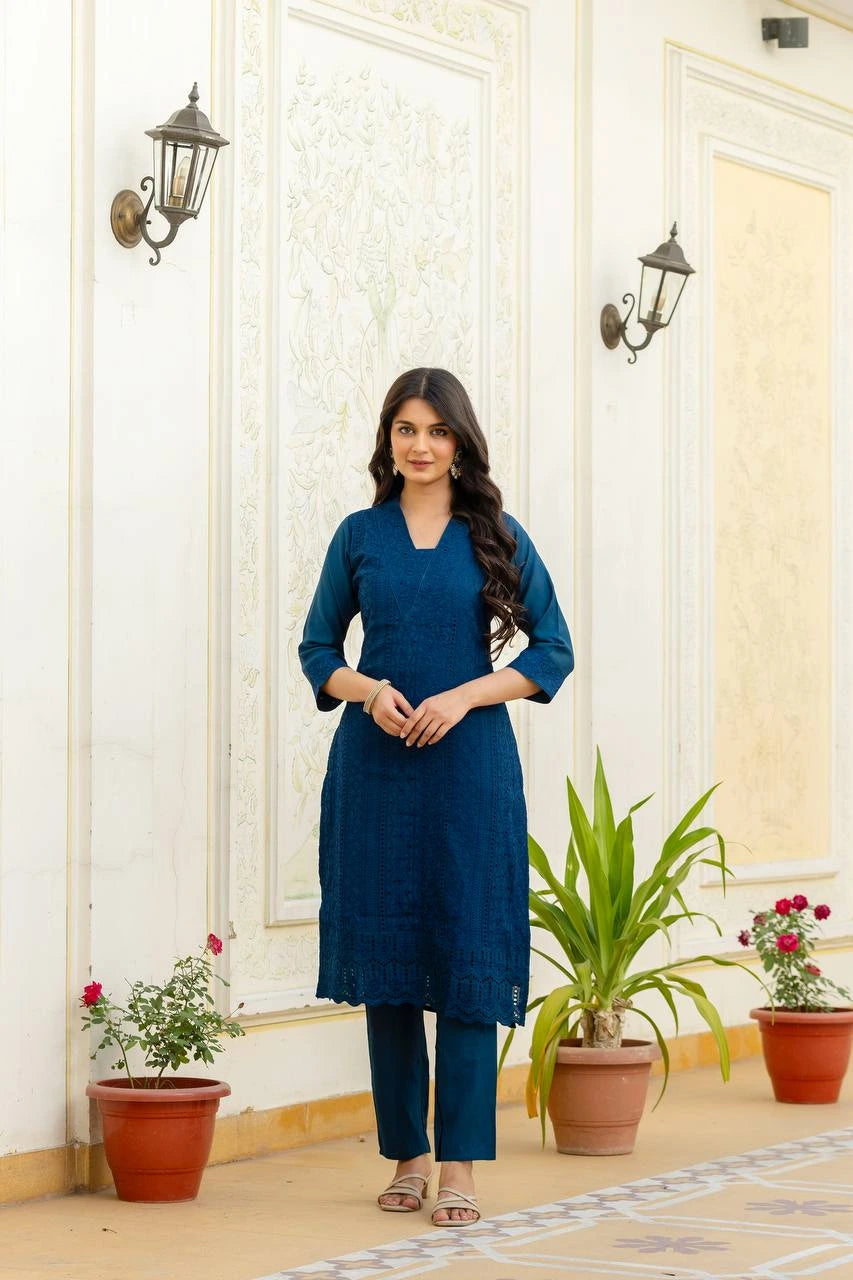 Woman in a blue outfit standing in a decorative indoor setting with plants.