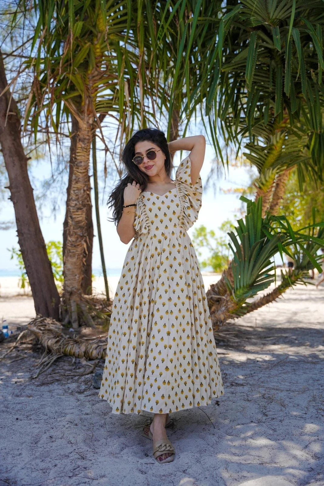 Woman in a polka dot dress standing under palm trees on a beach.
