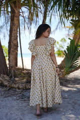 Woman in a polka dot dress standing in a tropical setting with palm trees.