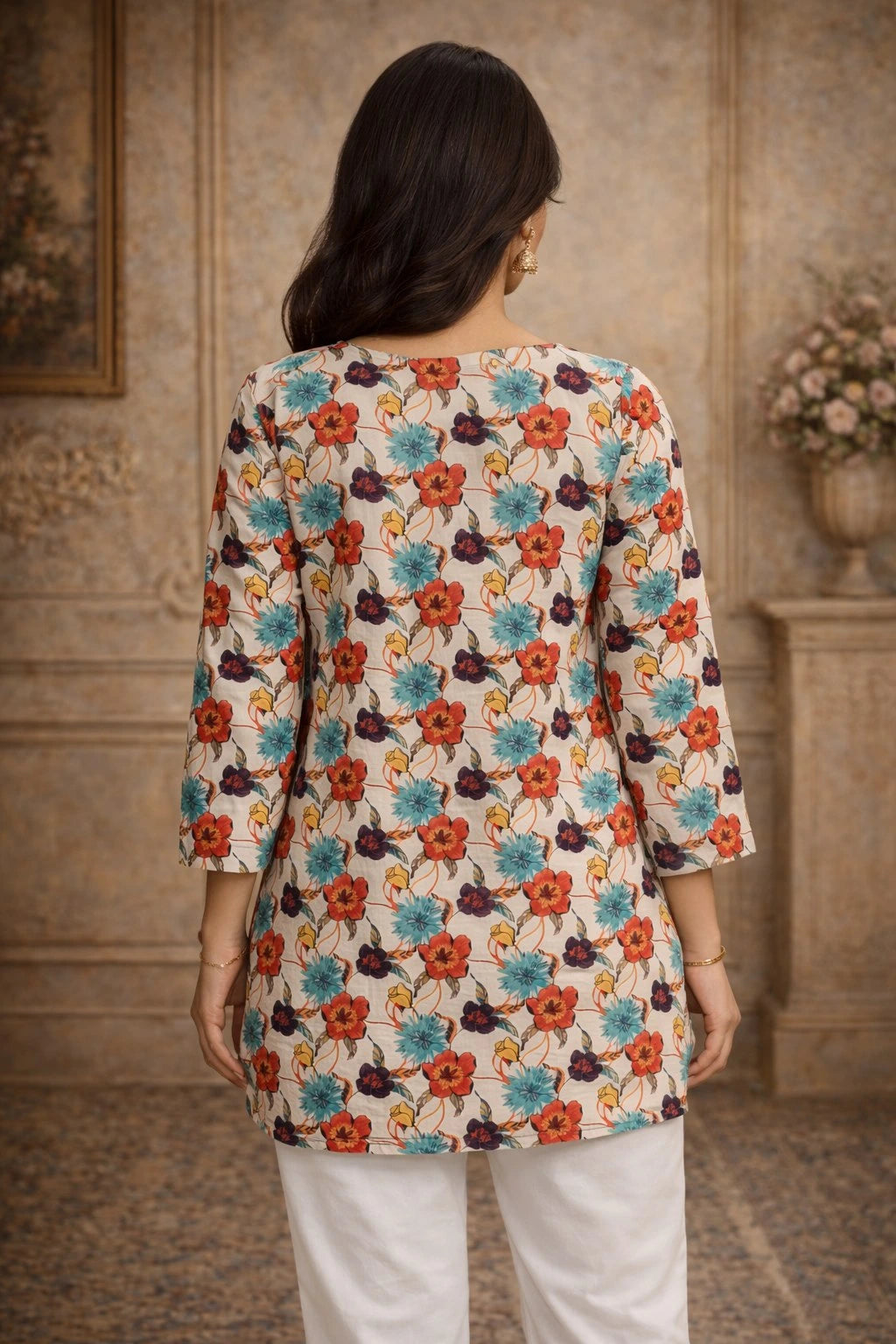 Woman wearing a floral patterned top in a room with wooden walls and a vase.