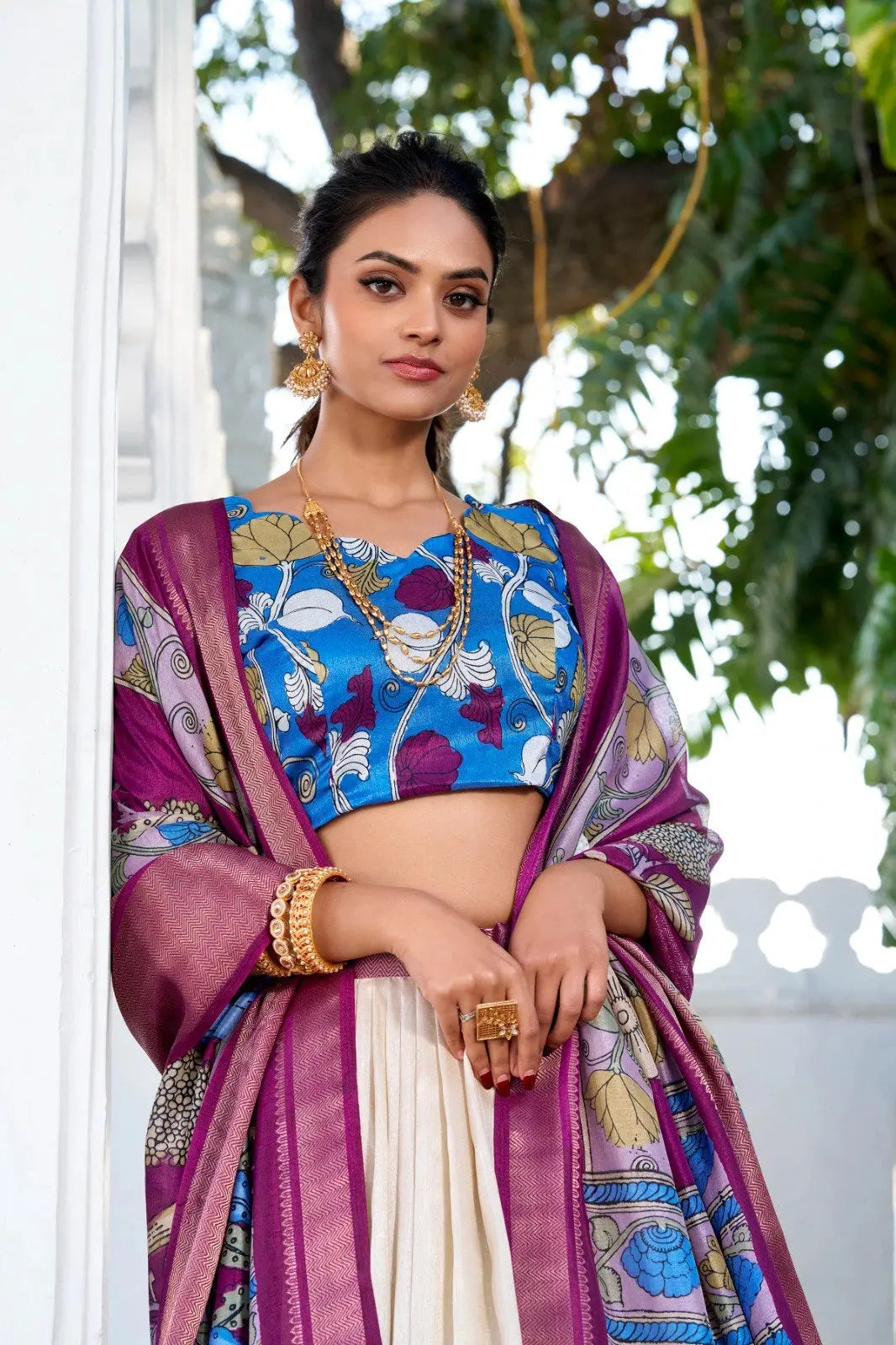 Elegant cream floral print lehenga with a blue embroidered blouse and rich purple woven dupatta for festive occasions.