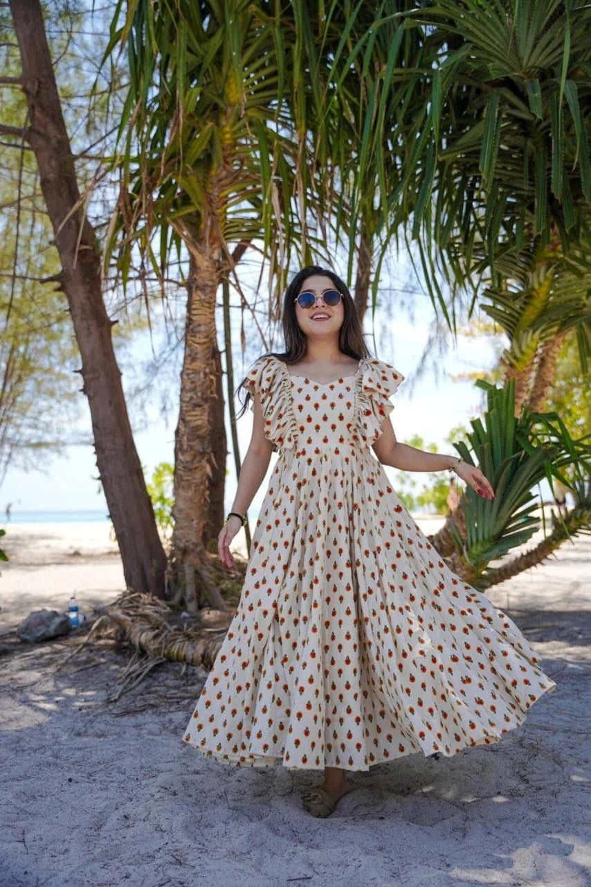 Woman in a polka dot dress standing under palm trees on a beach.
