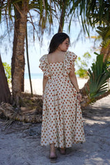 Woman in a polka dot dress standing on a sandy beach with palm trees in the background