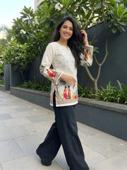 Woman wearing a patterned top and black pants standing outdoors with greenery in the background