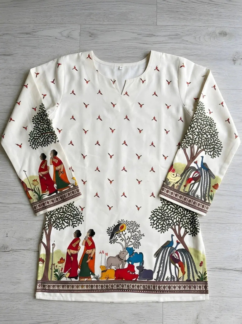 White long-sleeve top with colorful printed design on a gray wooden surface