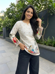 Woman wearing a white embroidered top with colorful patterns outdoors.