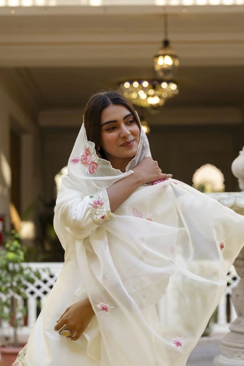 Woman wearing a white embroidered dupatta with pink flowers in an indoor setting.