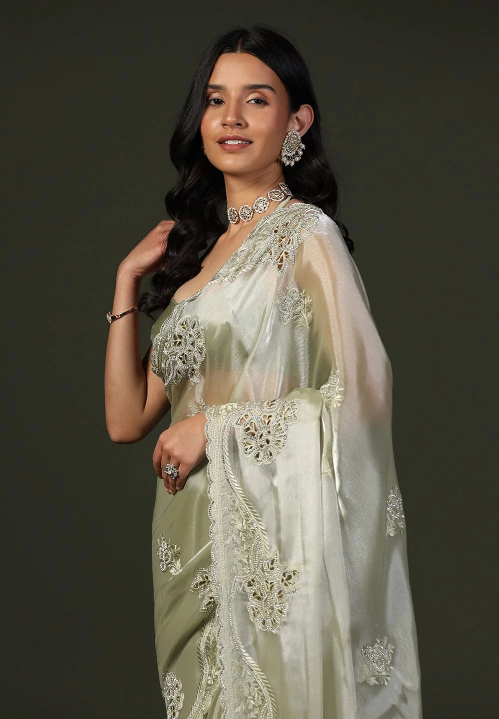 Woman wearing a white saree with intricate designs on a dark background