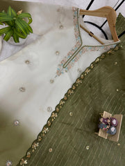 Green embroidered garment on a hanger with a small model of a family sitting on a box.