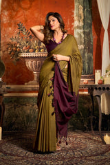 Woman in a green and purple saree standing in an ornate room with classical decor.