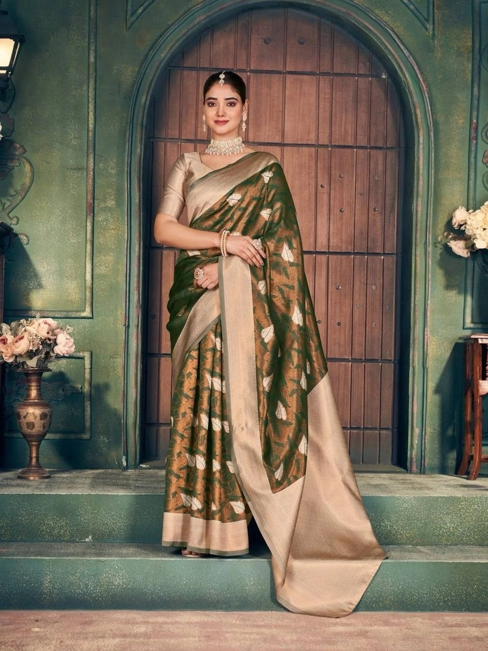 Woman in a traditional saree standing in an elegant indoor setting with decorative elements.