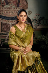 Woman in a green saree with gold jewelry against an ornate wall.