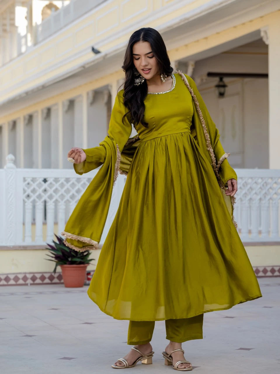Woman in a green traditional outfit standing in front of a building with white columns.