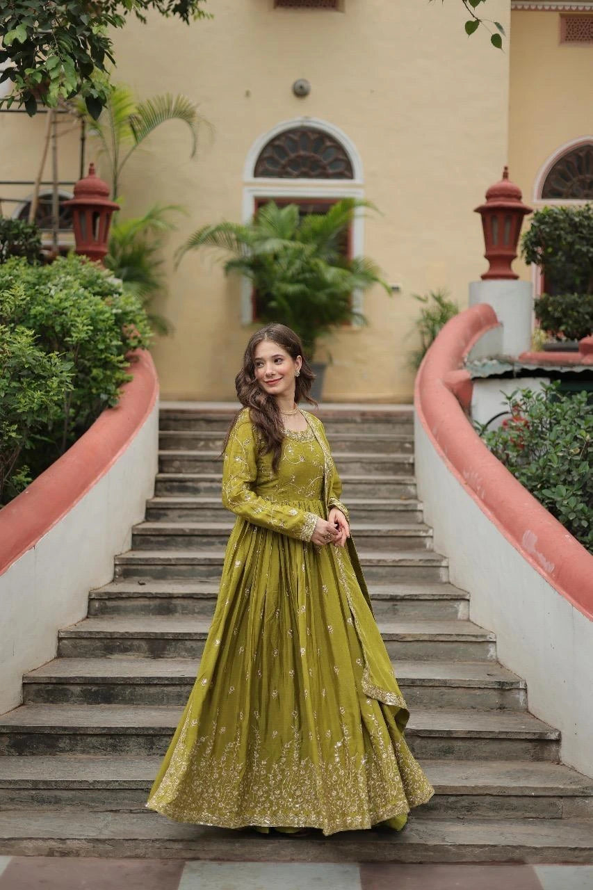 Woman in a green traditional outfit standing on a staircase with a building and plants in the background