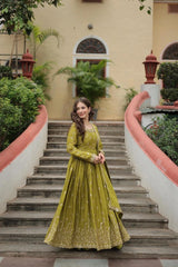 Woman in a green traditional outfit standing on a staircase with a building and plants in the background