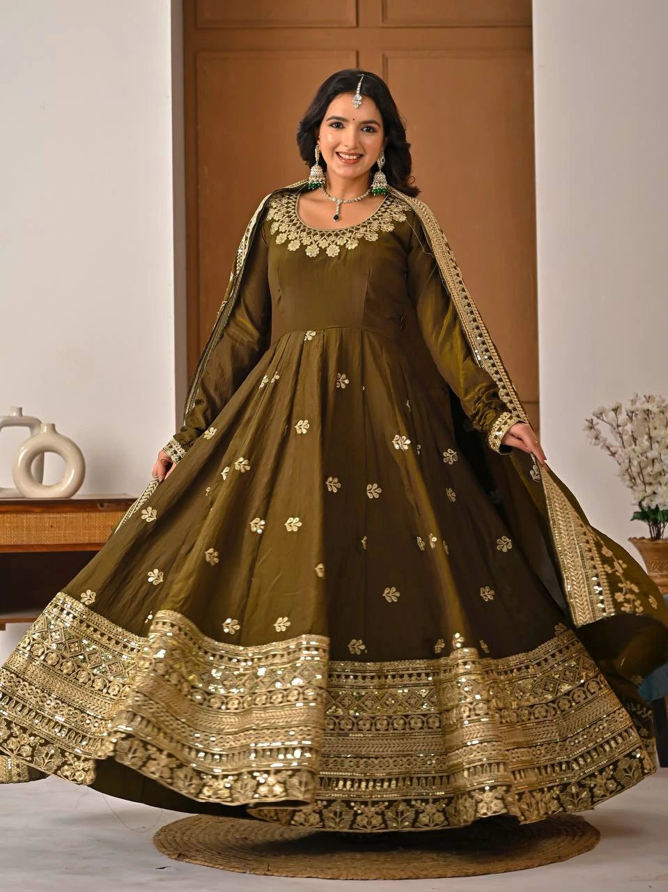 Woman wearing a traditional olive green and gold embroidered dress indoors.