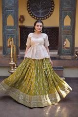 Woman in a traditional outfit with a green and gold skirt and white top, standing in an ornate room.