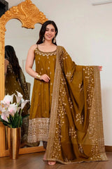 Woman in a traditional mustard yellow outfit with floral patterns standing in front of a decorative mirror.