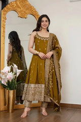 Woman in a green traditional outfit standing in front of a decorative mirror with flowers on the floor.