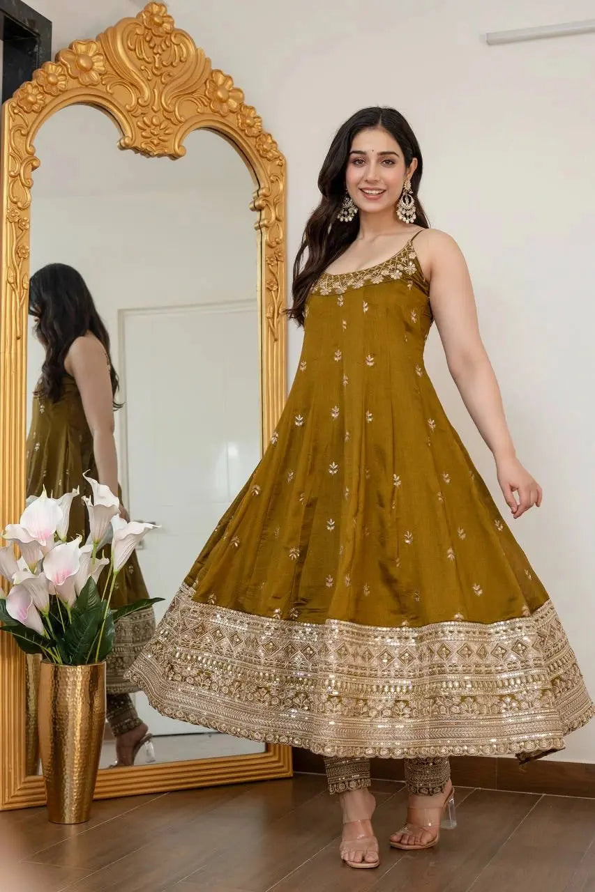 Woman in a mustard yellow traditional outfit standing in front of a decorative mirror.