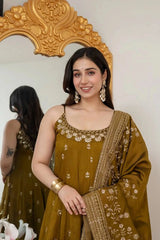 Woman in a mustard yellow traditional outfit with floral patterns standing in front of a decorative mirror.