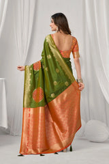 Woman wearing a green and orange saree with a white curtain background